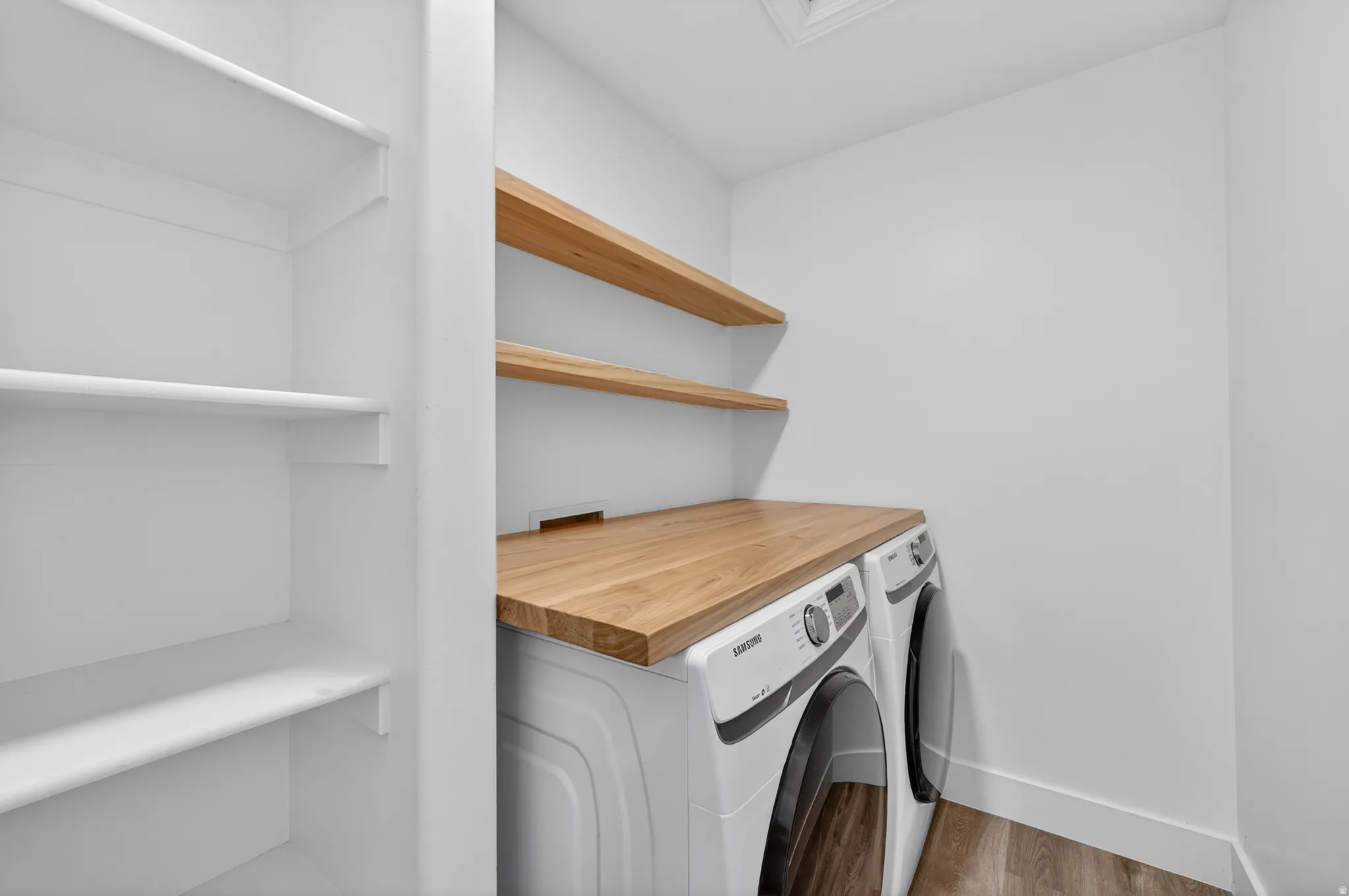 Laundry area featuring a wood-finish countertop, white built-in shelving, and two floating wood-finish shelves
