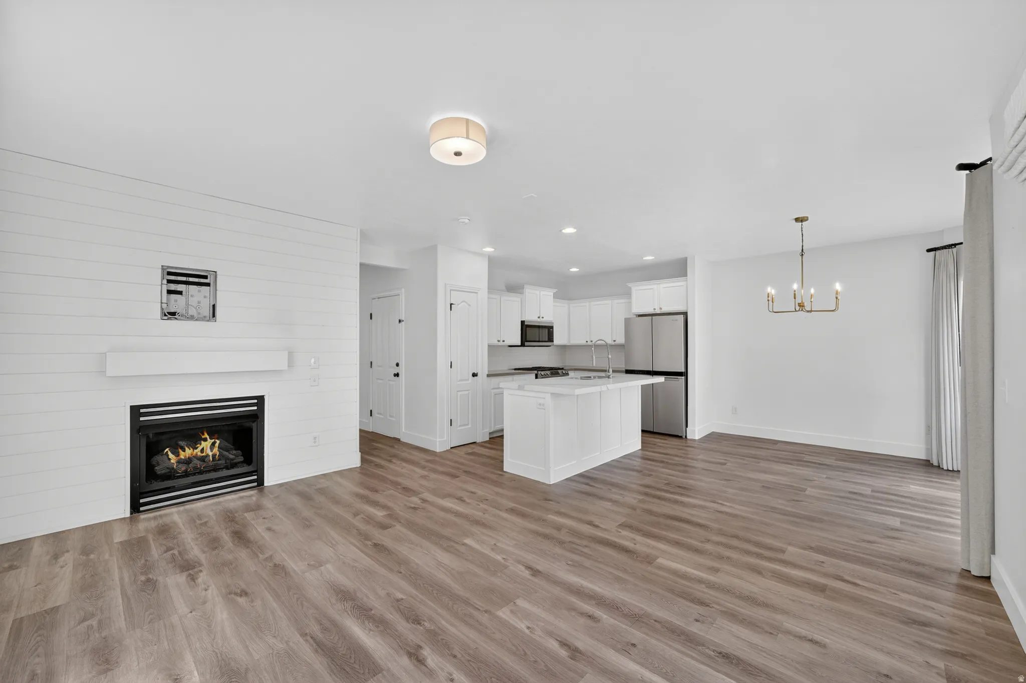 Open-concept living space with wood-finish flooring, a contemporary fireplace with shiplap-style surround, a kitchen island, and stainless steel appliances