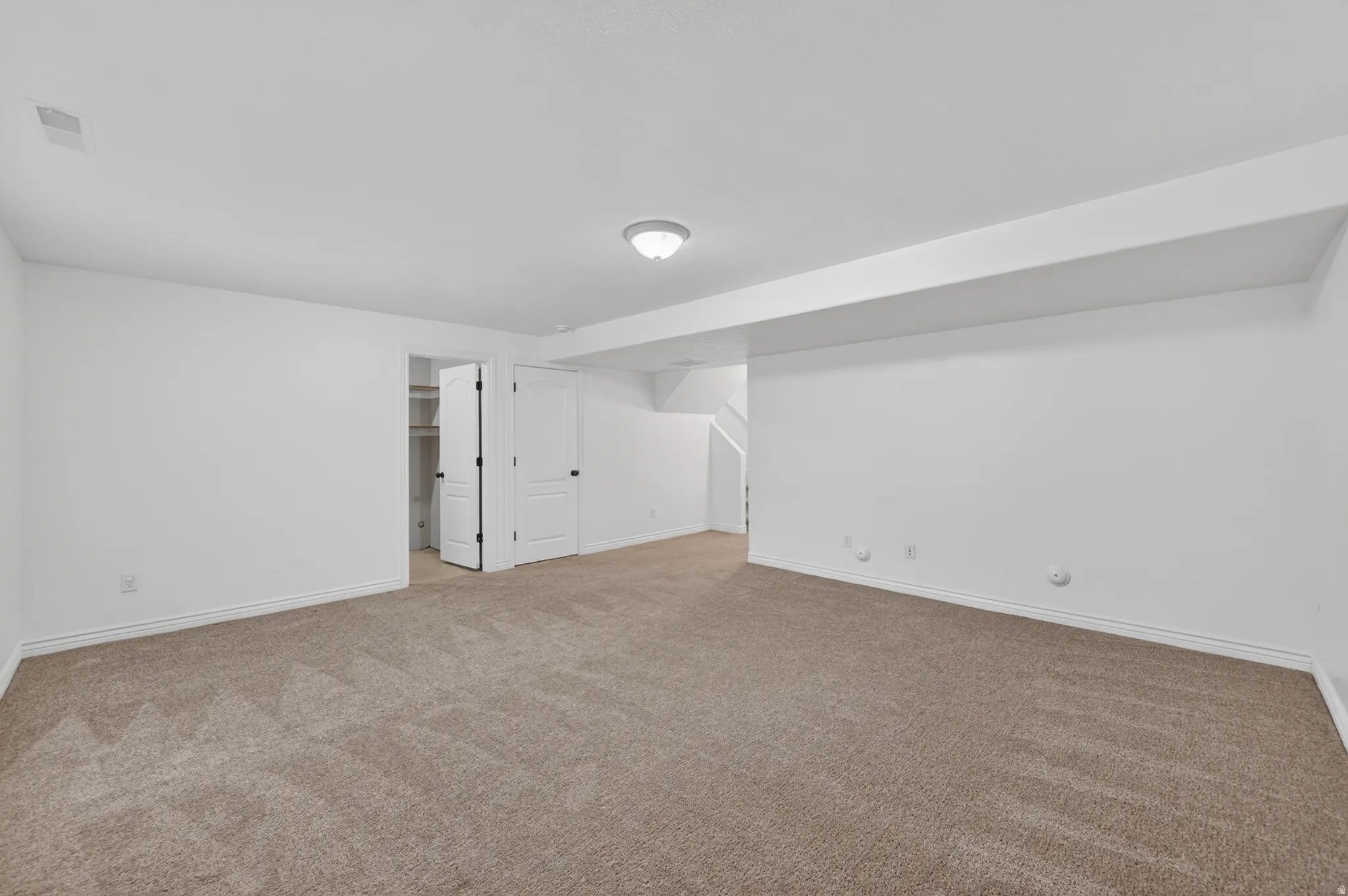 Spacious room featuring neutral carpeting, white walls, and a flush-mount ceiling light