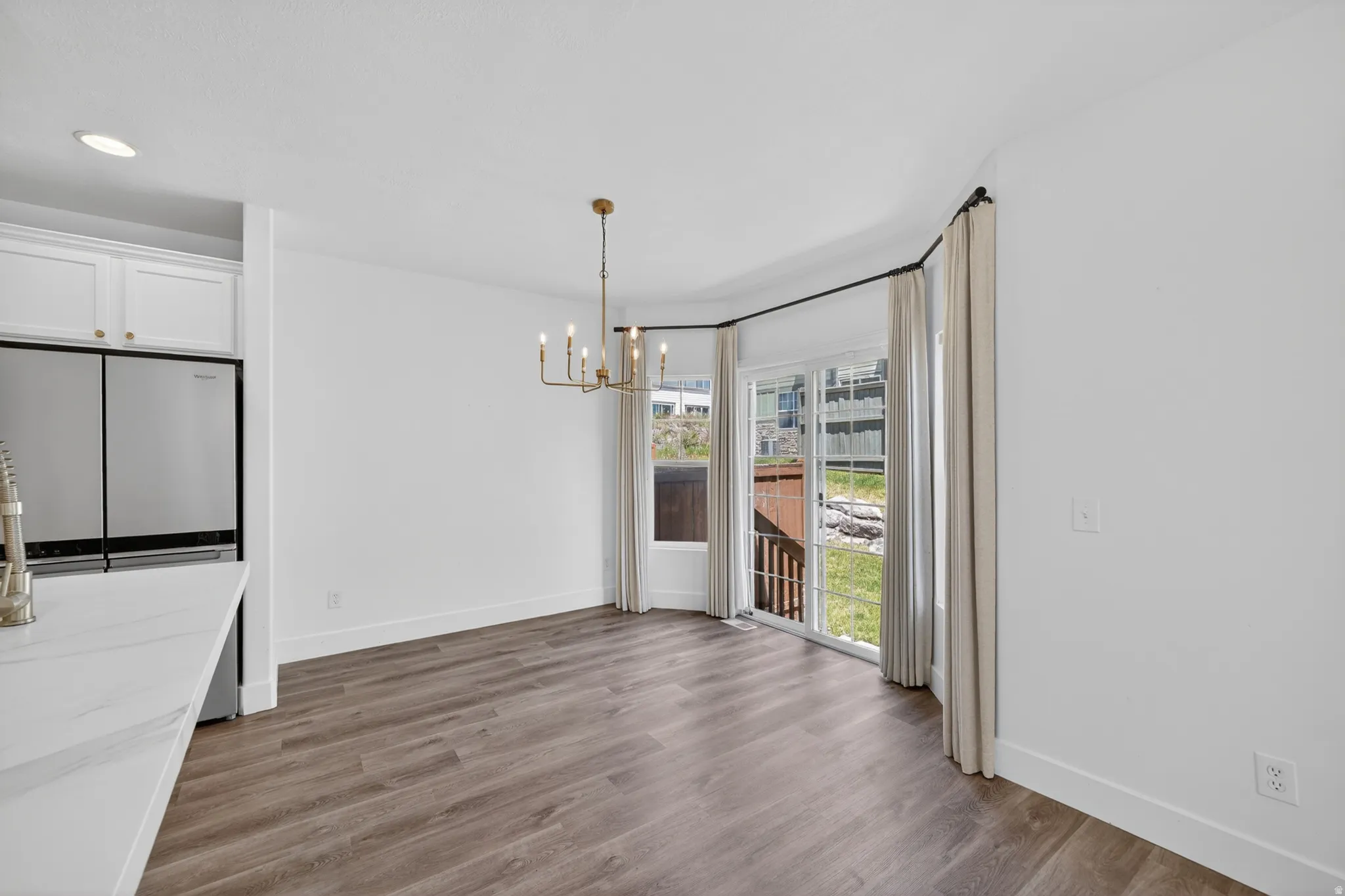 Bright dining area featuring wood-finish flooring, a contemporary gold chandelier, and direct access to an outdoor deck through sliding glass doors