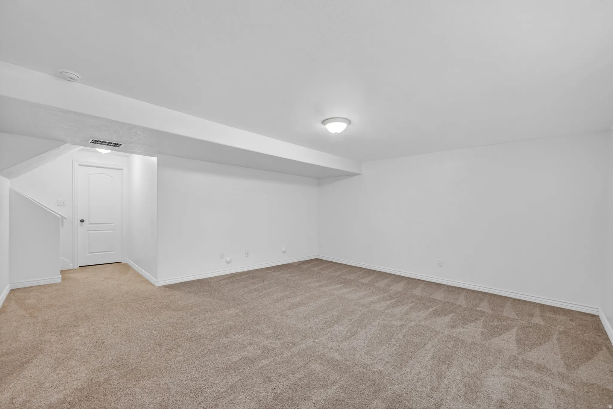 Spacious carpeted room featuring a neutral color palette, white walls, and a white ceiling with a flush-mount light fixture