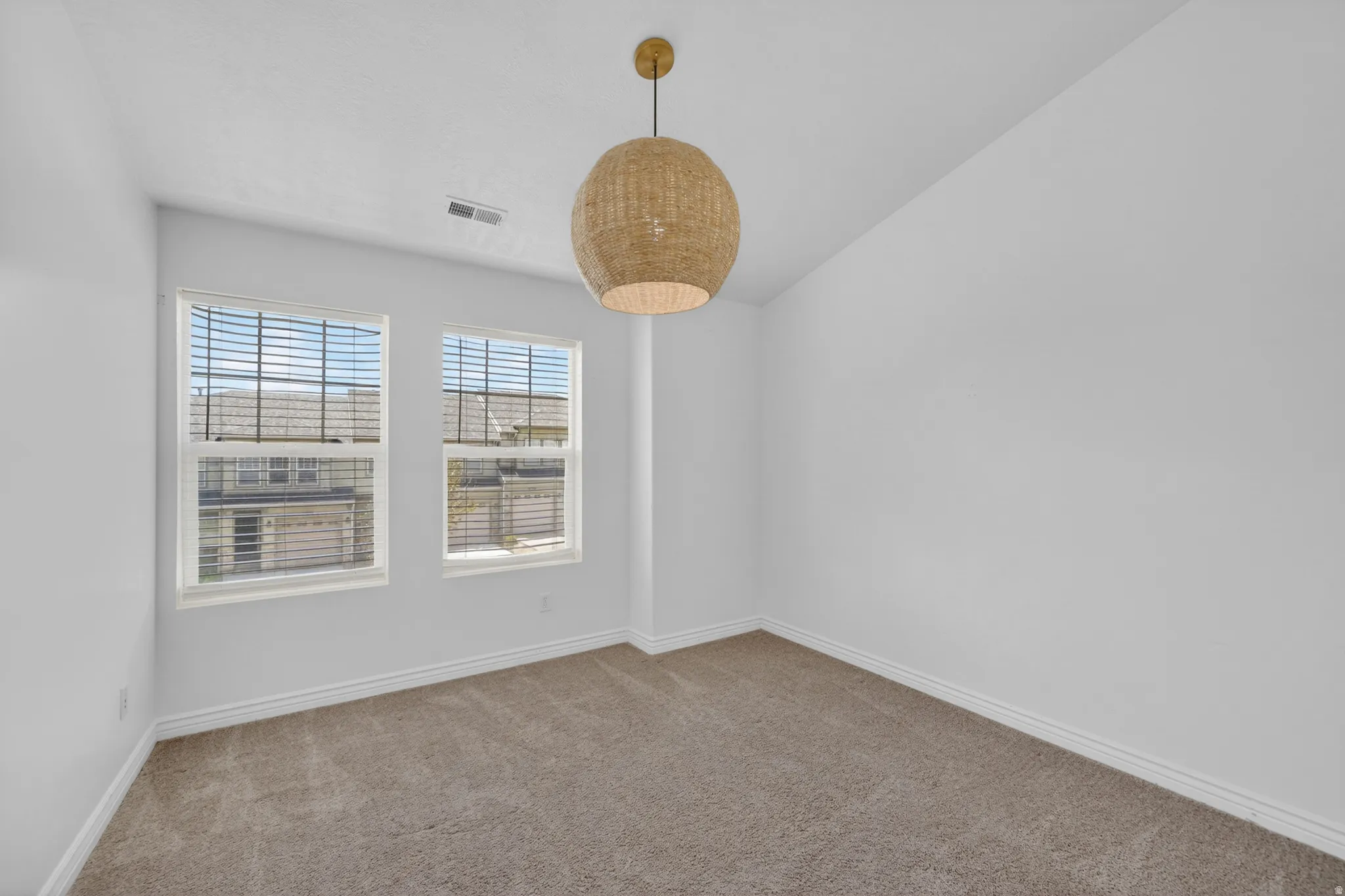 Room featuring two white-framed windows with blinds, a woven pendant light fixture, light gray carpet, and white baseboards