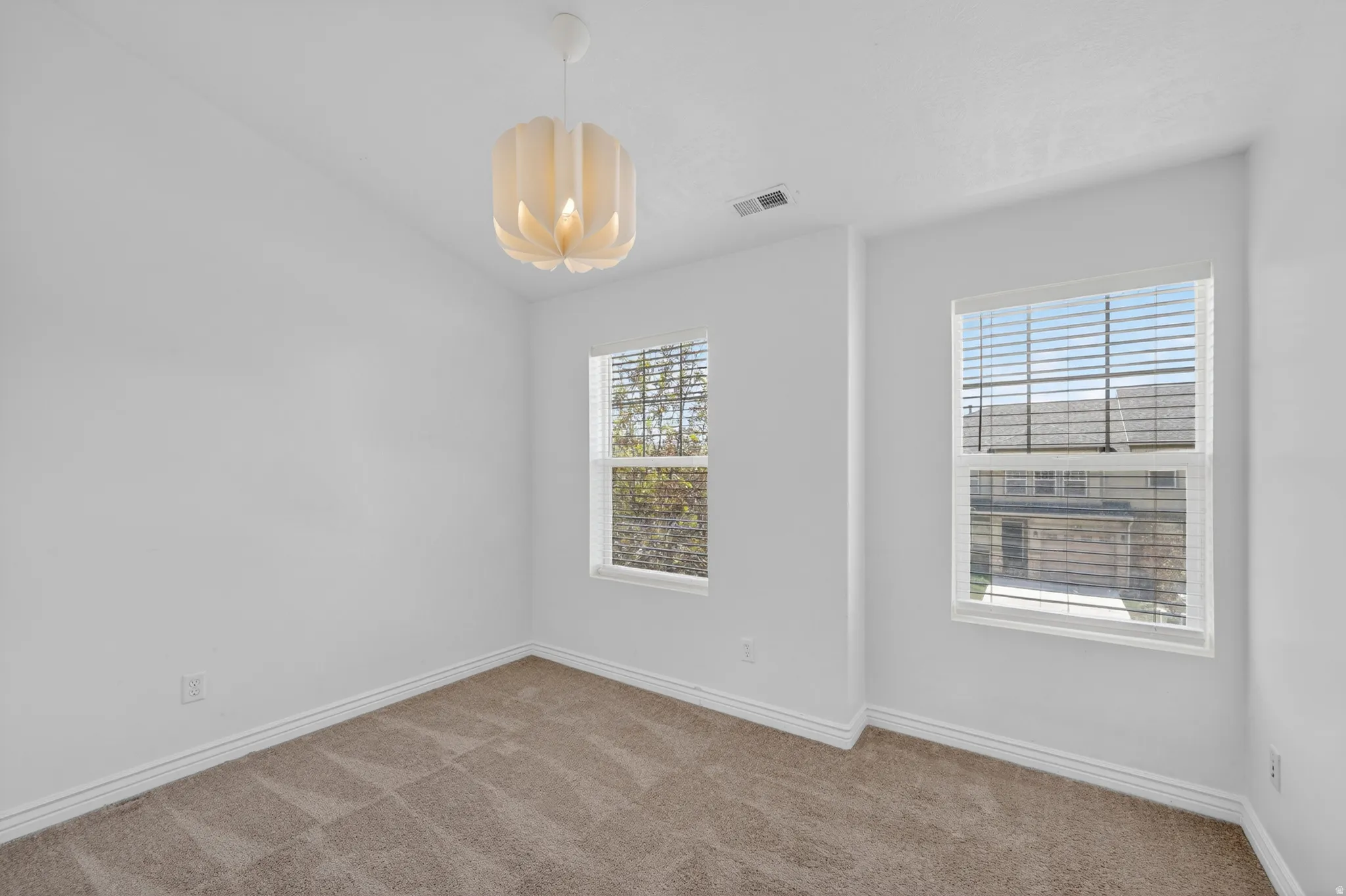 Neutral painted walls featuring two windows with horizontal blinds, textured carpet flooring, and a contemporary ceiling light fixture