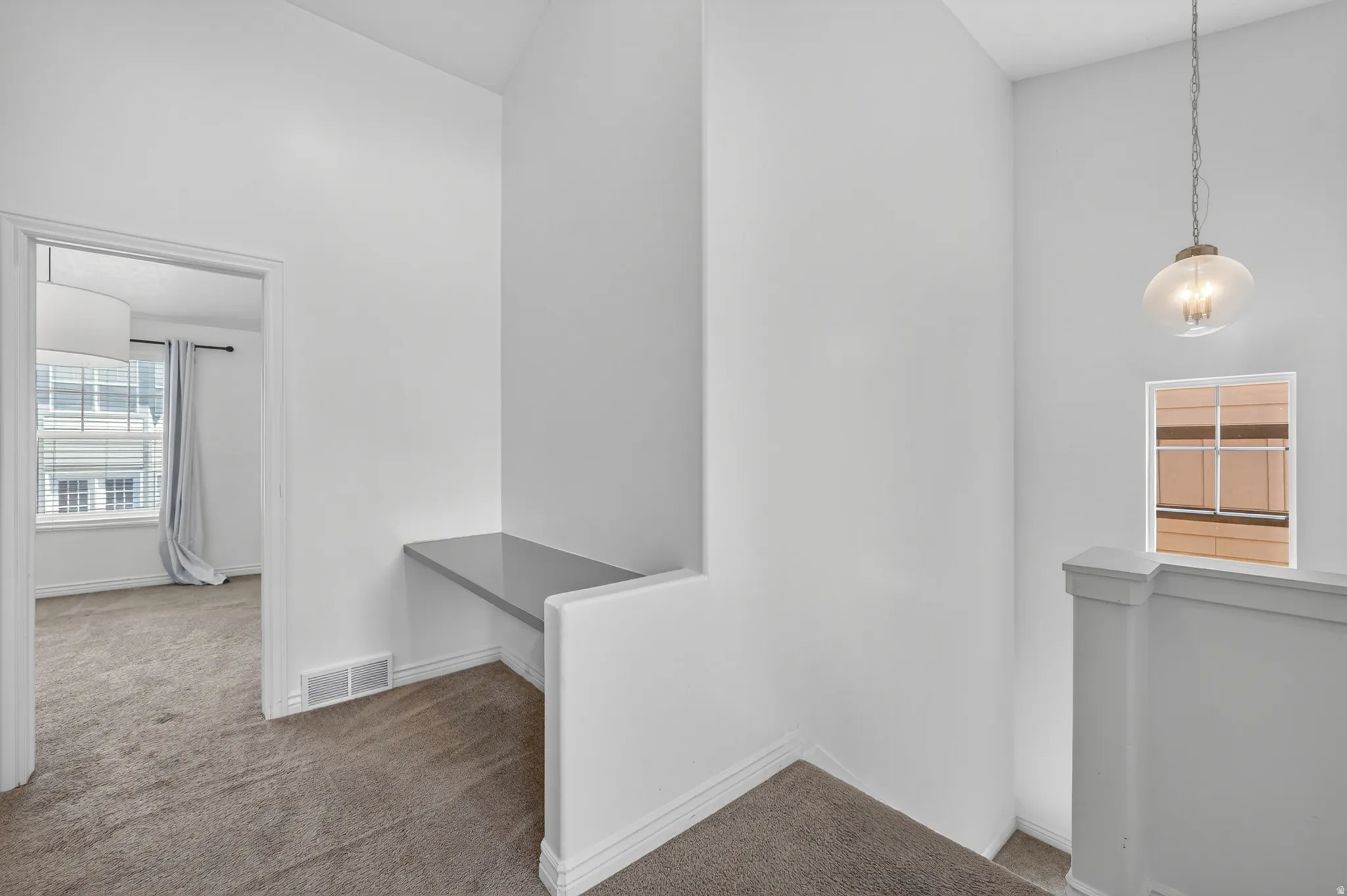 Loft area featuring a built-in desk with a gray surface, textured carpet flooring, and a contemporary glass pendant light fixture