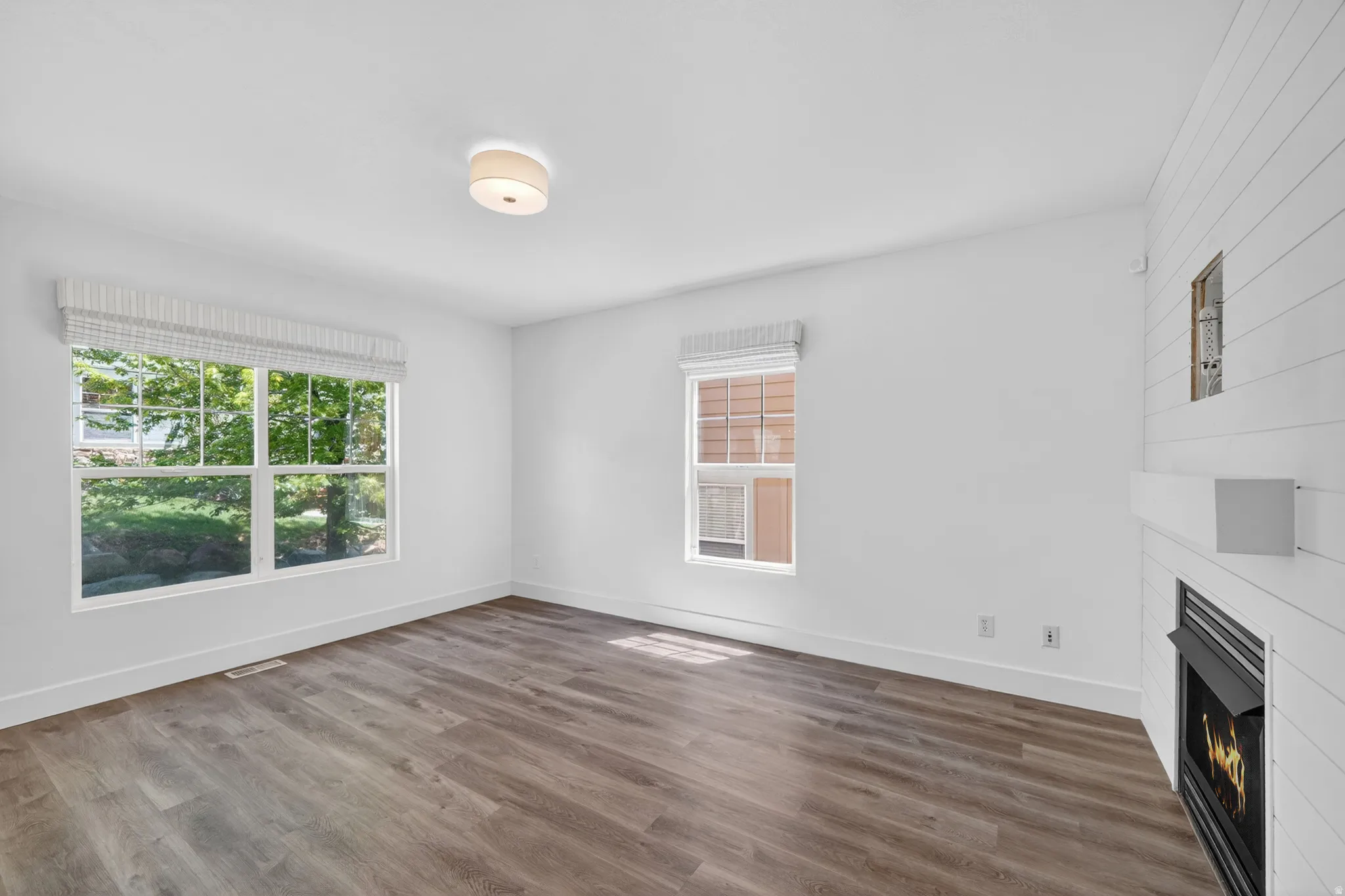 Spacious room featuring wood-finish flooring, white baseboards, and a fireplace with a white shiplap surround
