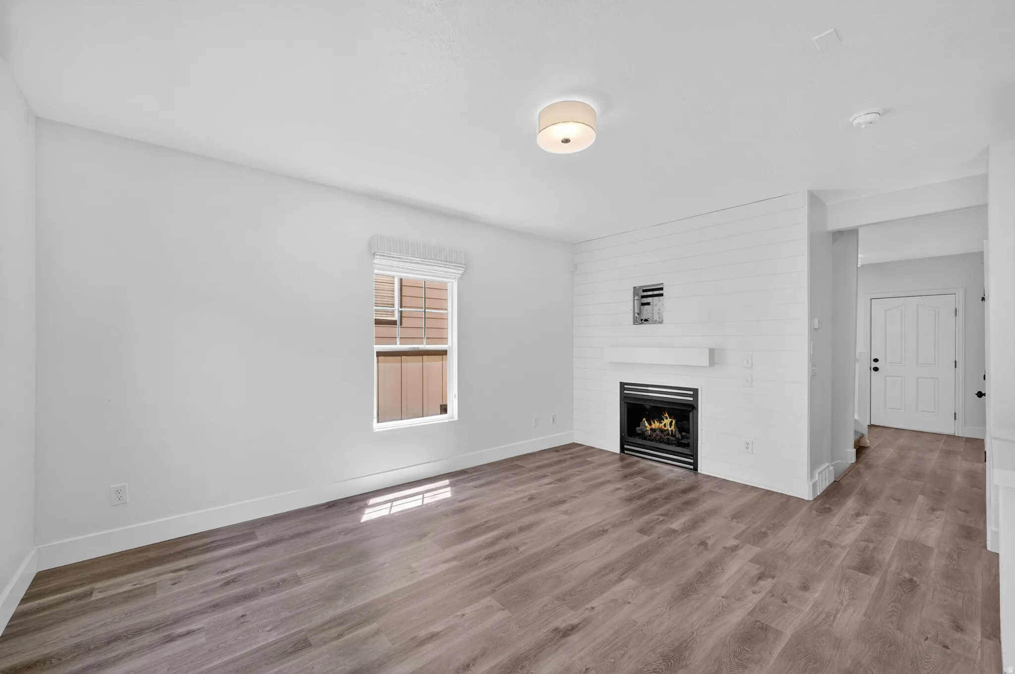 Living area featuring wood-finish flooring, a contemporary fireplace with a shiplap accent wall, and a built-in mantel