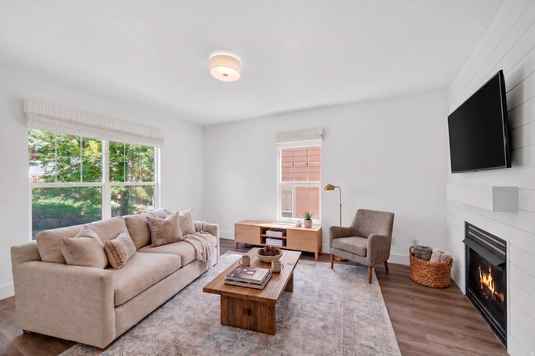 Living area featuring a shiplap accent wall with a built-in fireplace, wood-finish flooring, and large windows with privacy blinds