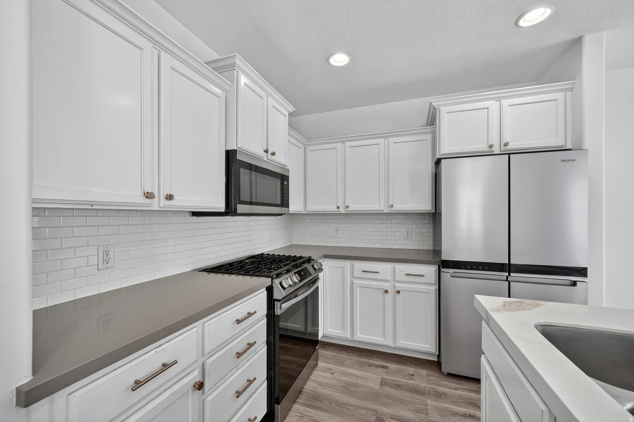 Modern kitchen featuring white shaker cabinetry, stainless steel appliances, a white subway tile backsplash, and light wood-finish flooring