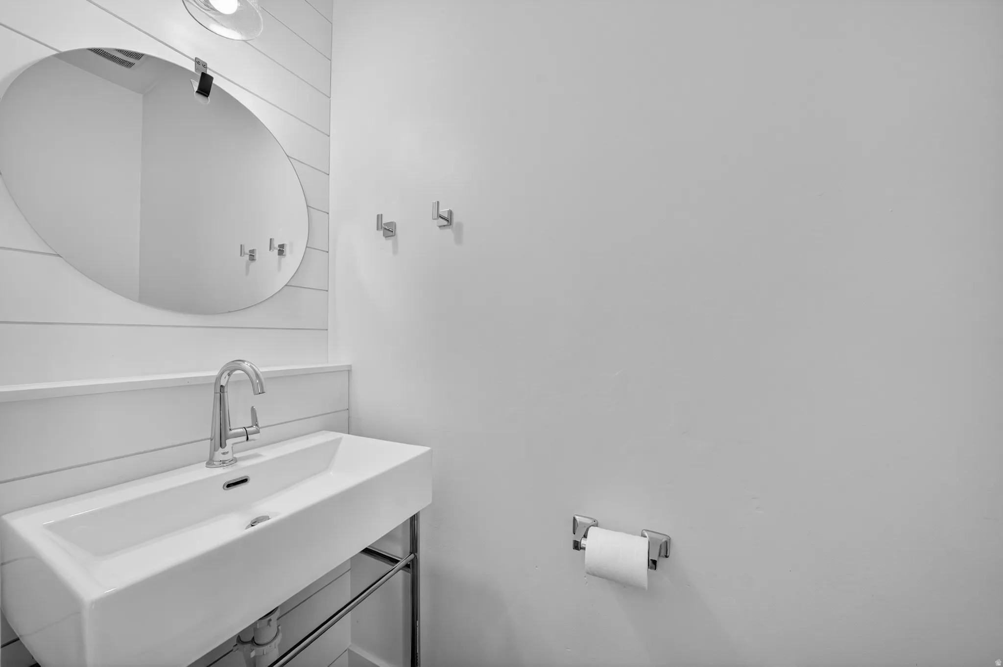 Modern rectangular sink with chrome faucet, complemented by a large oval mirror