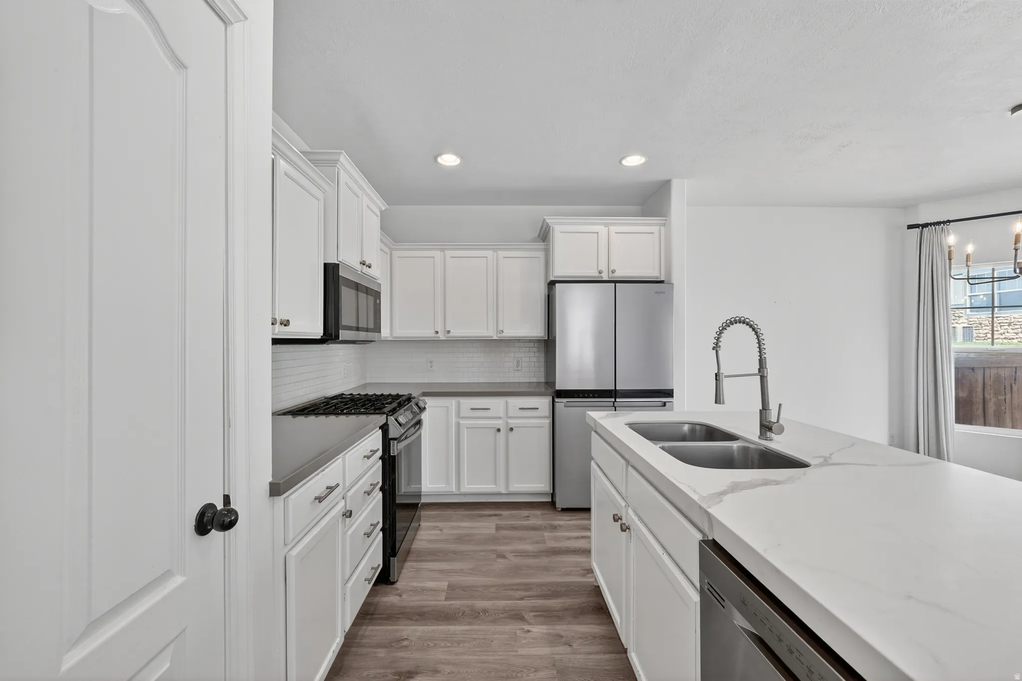 Kitchen featuring white shaker cabinetry, stainless steel appliances, a double basin sink, and wood-finish flooring