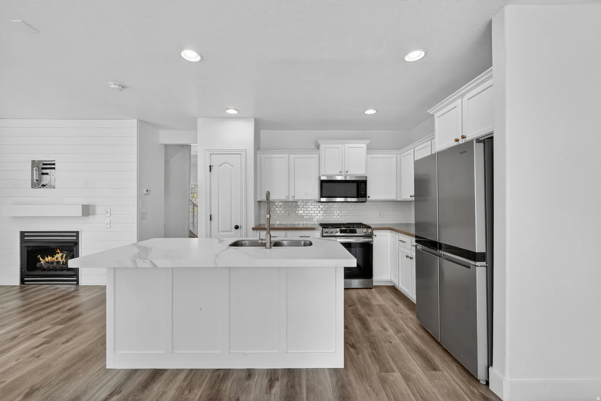 Kitchen featuring a large island with sink, stainless steel appliances, white cabinetry, and wood-finish flooring