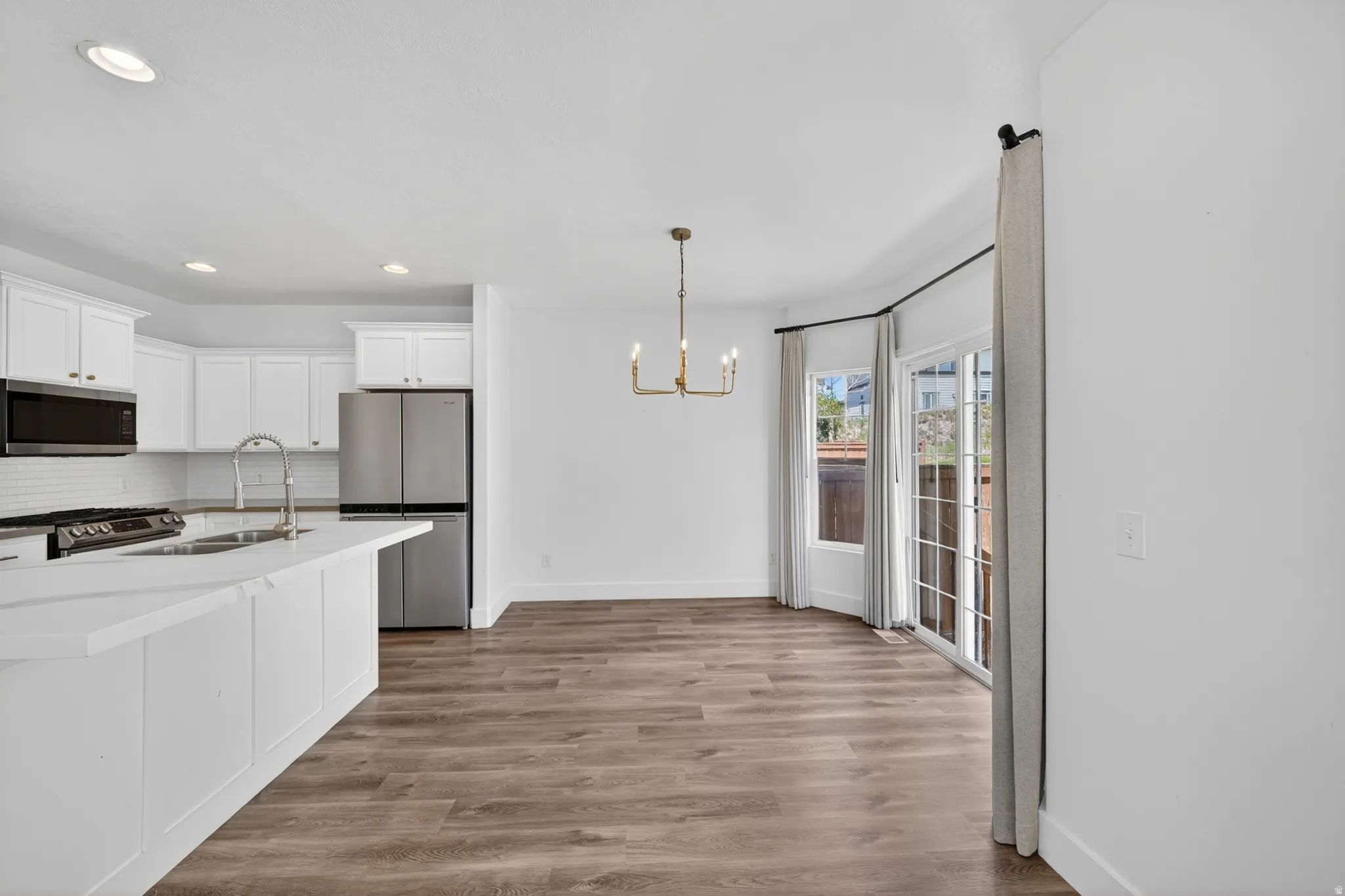 Open-concept kitchen and dining area featuring white cabinetry, stainless steel appliances, and wood-finish flooring