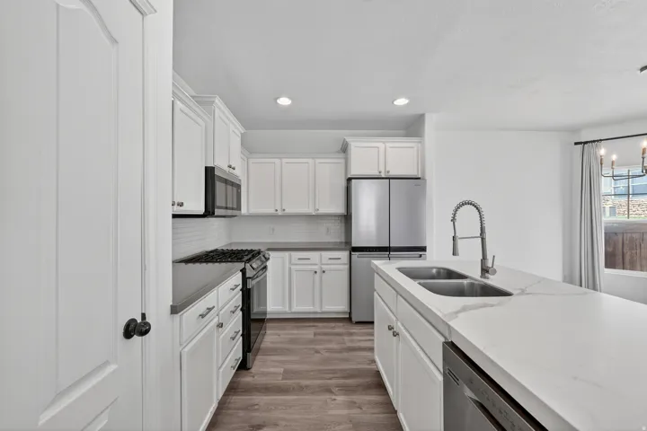 Kitchen featuring white shaker cabinetry, stainless steel appliances, a double basin sink, and wood-finish flooring