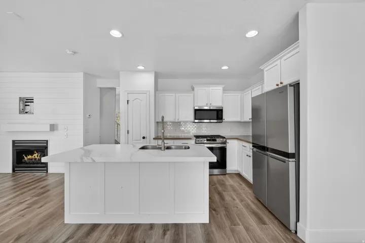 Kitchen featuring a large island with sink, stainless steel appliances, white cabinetry, and wood-finish flooring