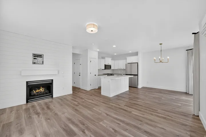 Open-concept living space with wood-finish flooring, a contemporary fireplace with shiplap-style surround, a kitchen island, and stainless steel appliances