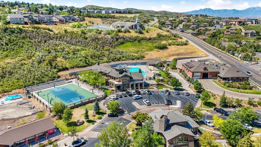 Expansive recreation area featuring a multi-sport court with spectator seating, a large outdoor swimming pool, and a clubhouse with stone and timber accents