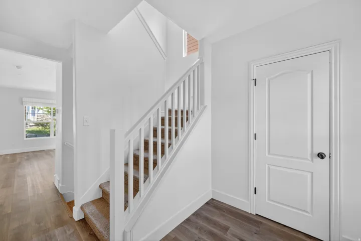 Modern entryway featuring wood-finish flooring, a carpeted staircase with white railings, and a two-panel interior door