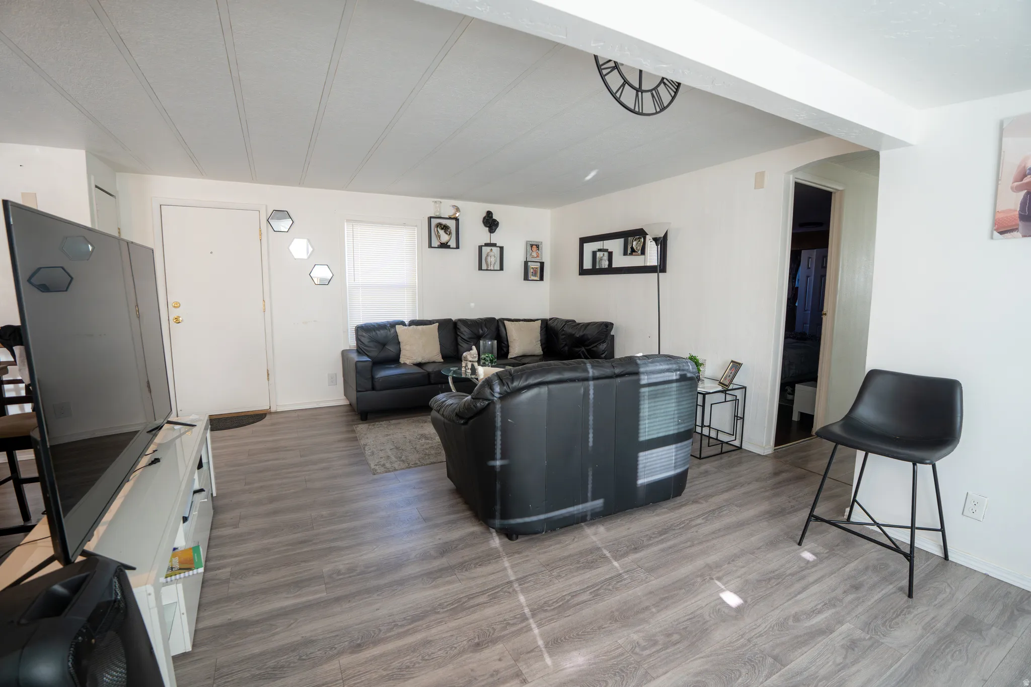 Spacious living area featuring wood-finish flooring, white walls, and a white ceiling with visible beams