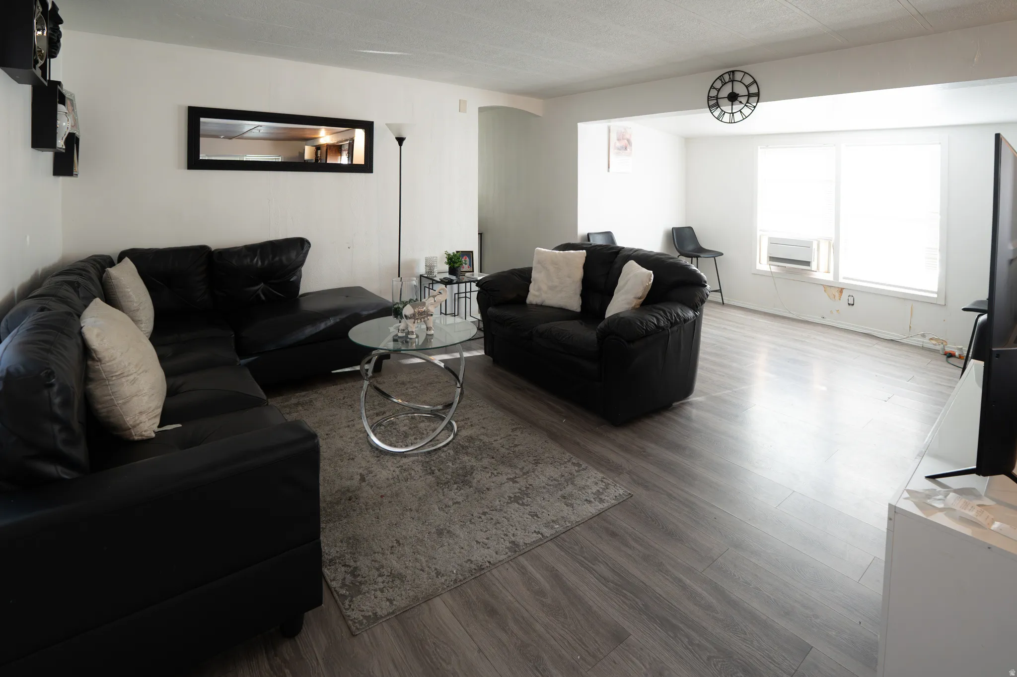 Open-concept living space with light wood-finish flooring, white walls, and a wide entryway to an additional area