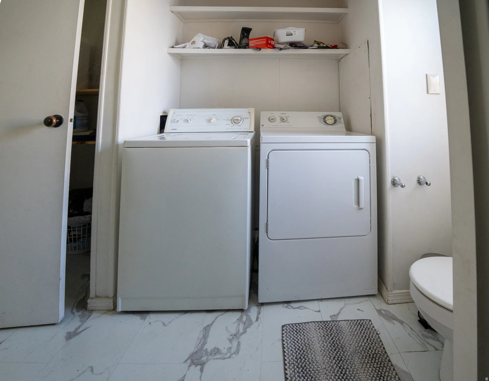 Dedicated laundry area featuring a white top-load washing machine, white front-load dryer, and overhead shelving