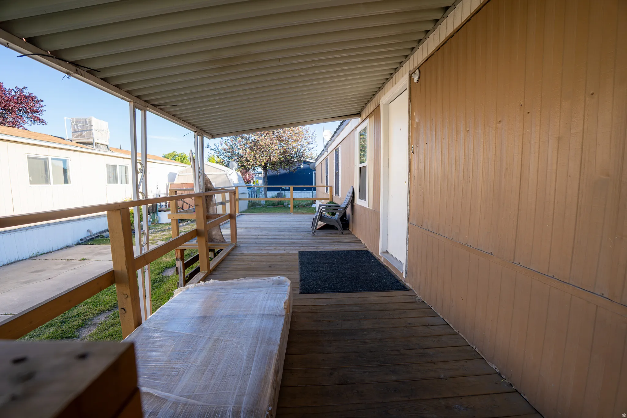 Covered wooden deck with a light brown vertical siding exterior, white entry door, and multiple windows