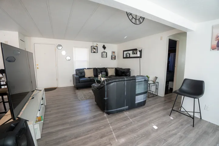 Spacious living area featuring wood-finish flooring, white walls, and a white ceiling with visible beams