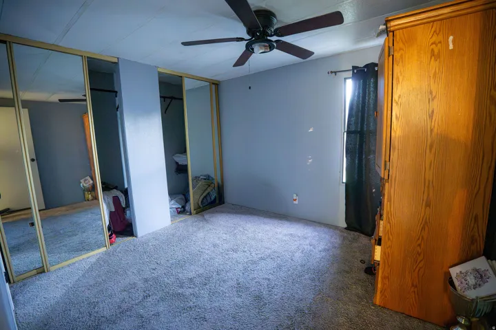 Room featuring wall-to-wall carpeting, light blue wall paint, a ceiling fan with dark blades, and mirrored sliding closet doors