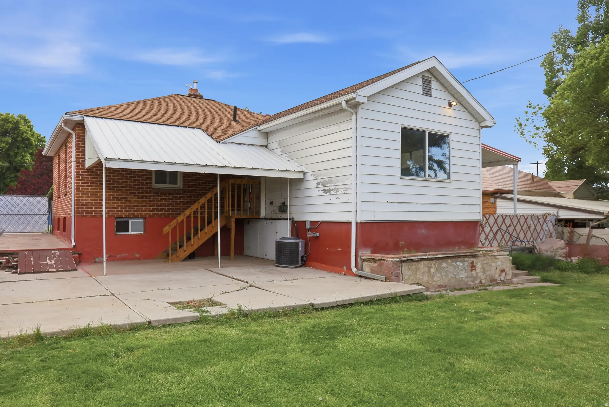 Rear exterior featuring a concrete patio, brick and siding facade, and a covered deck with wooden stairs