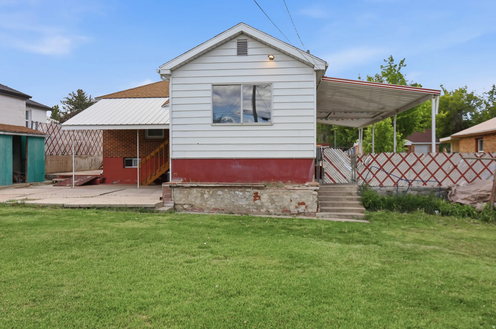 Expansive rear yard featuring a manicured lawn, concrete patio, and a covered carport with a metal roof