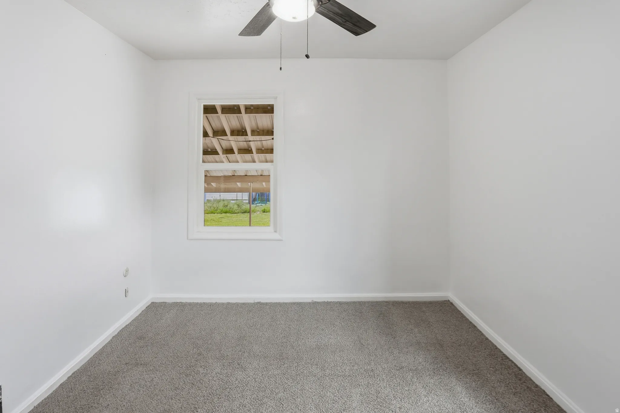 Room featuring light gray carpeting, crisp white walls, a white-framed window, and a ceiling fan with dark wood-finish blades