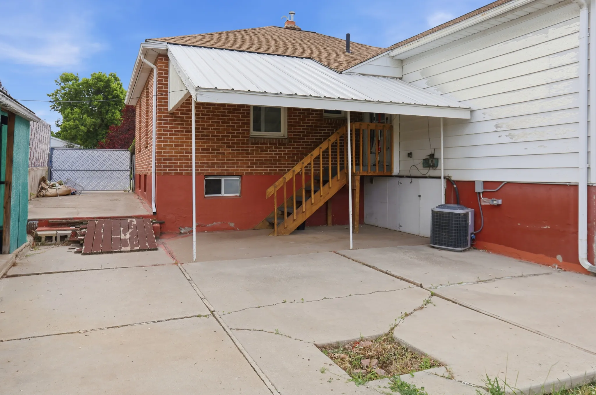 Concrete patio area featuring a covered porch with a metal roof, exterior brick siding, wood staircase, and vinyl siding