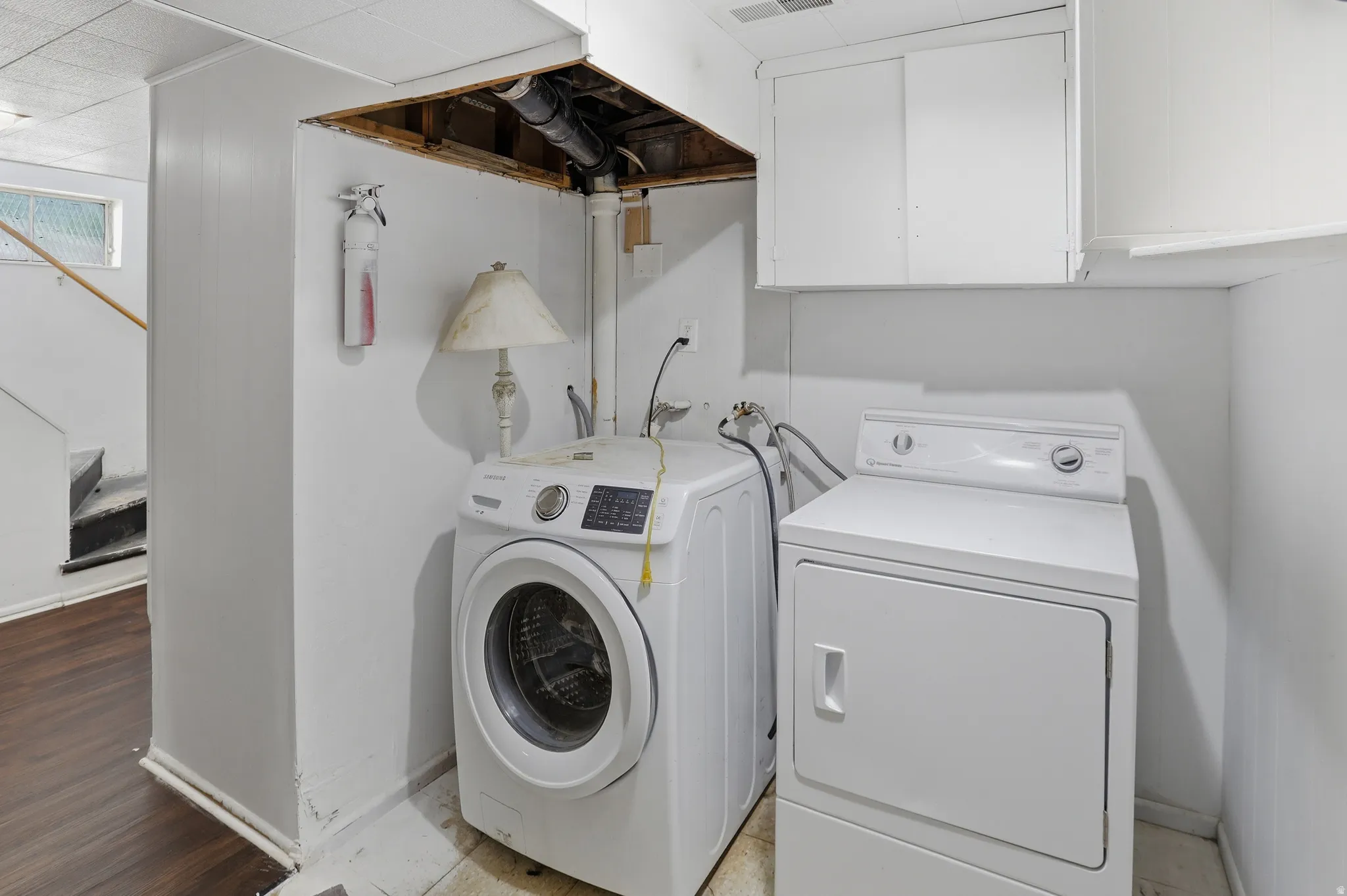 Dedicated laundry area featuring a washer and dryer, white cabinetry, and wood-finish flooring extending into the adjacent space