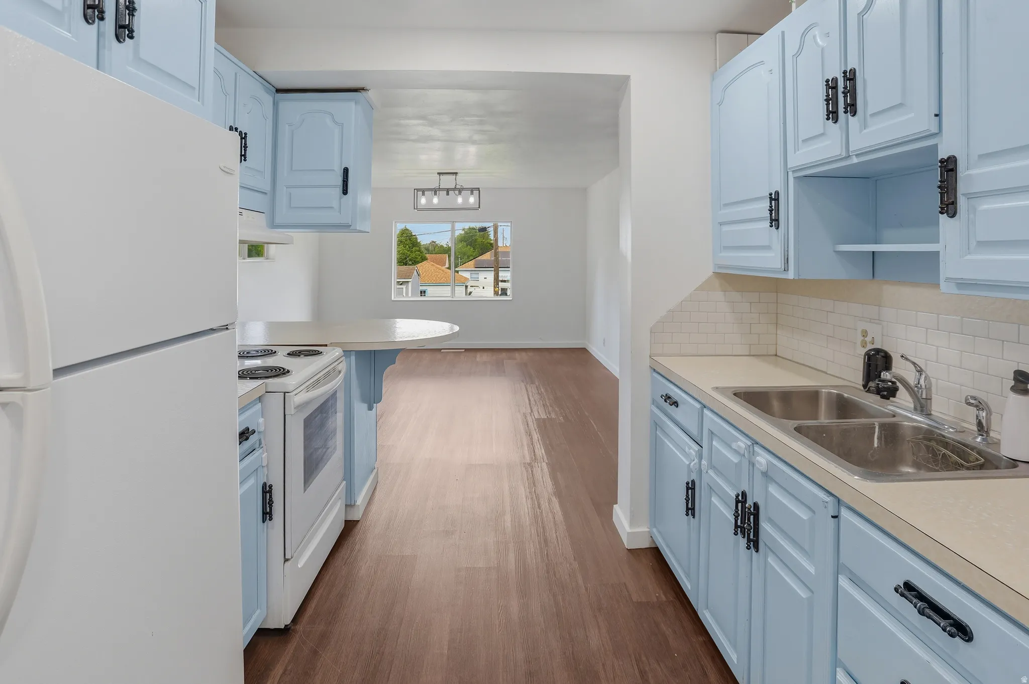 Kitchen featuring light blue cabinetry with dark hardware, white subway tile backsplash, and a double basin stainless steel sink