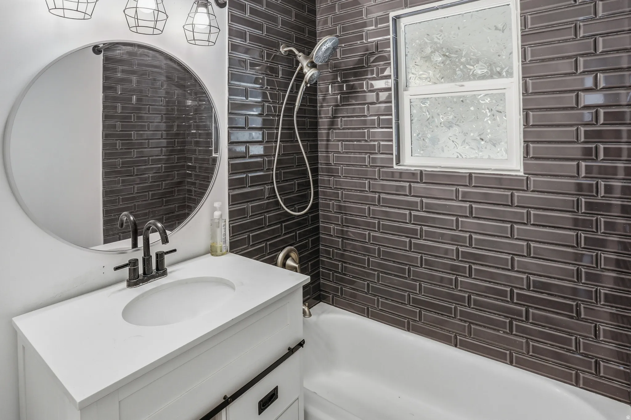 Bathroom featuring dark subway tile shower surround, white bathtub, and a modern vanity with integrated sink