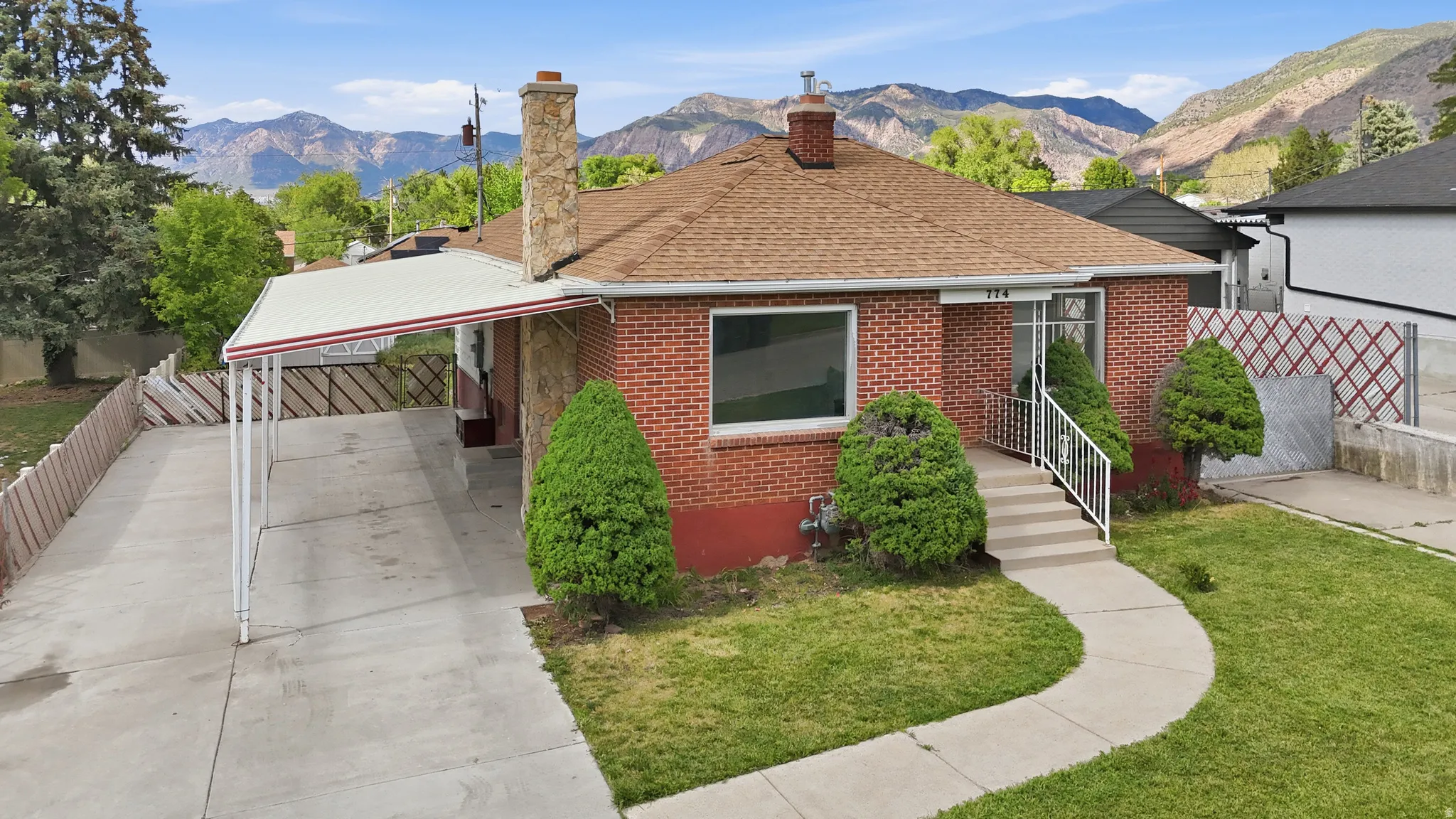 Brick exterior residence featuring a brown shingle roof, a covered carport, and a concrete pathway leading to the front entry