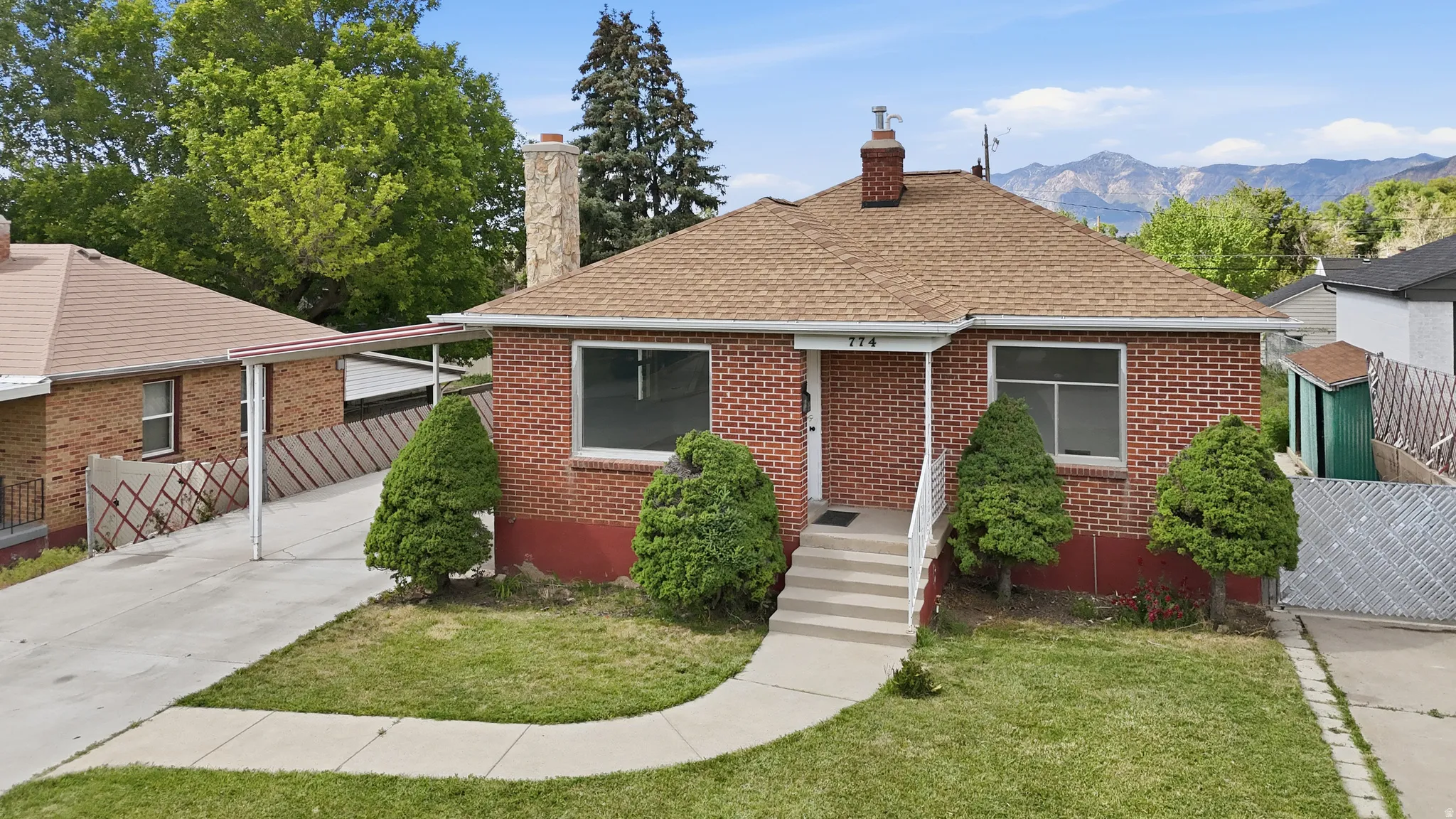 Red brick exterior featuring a brown shingle roof and a concrete walkway