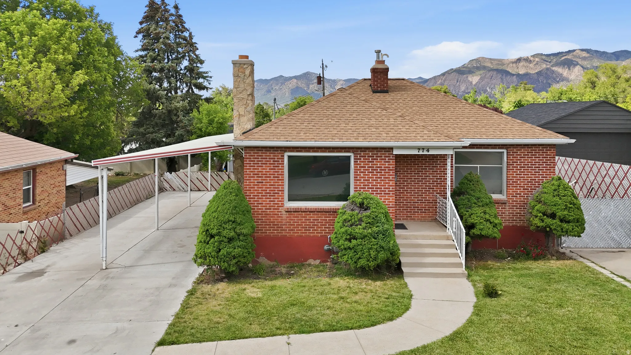 Brick exterior residence featuring a front entry with concrete steps and white railings, a covered carport, and a prominent chimney