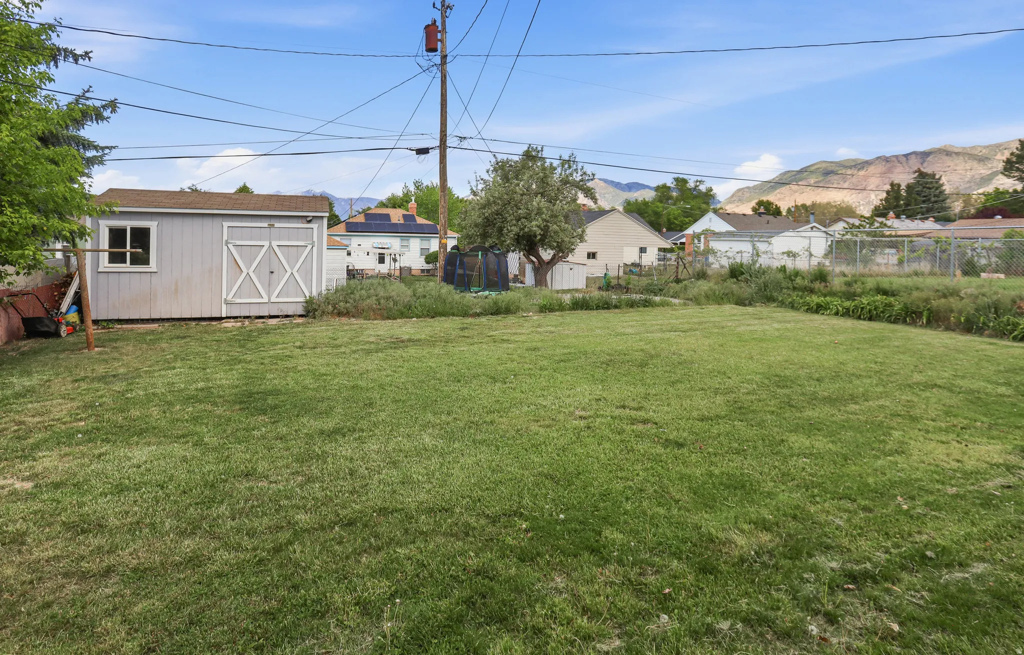 Expansive grassy yard area featuring a detached storage shed with a window and double barn doors