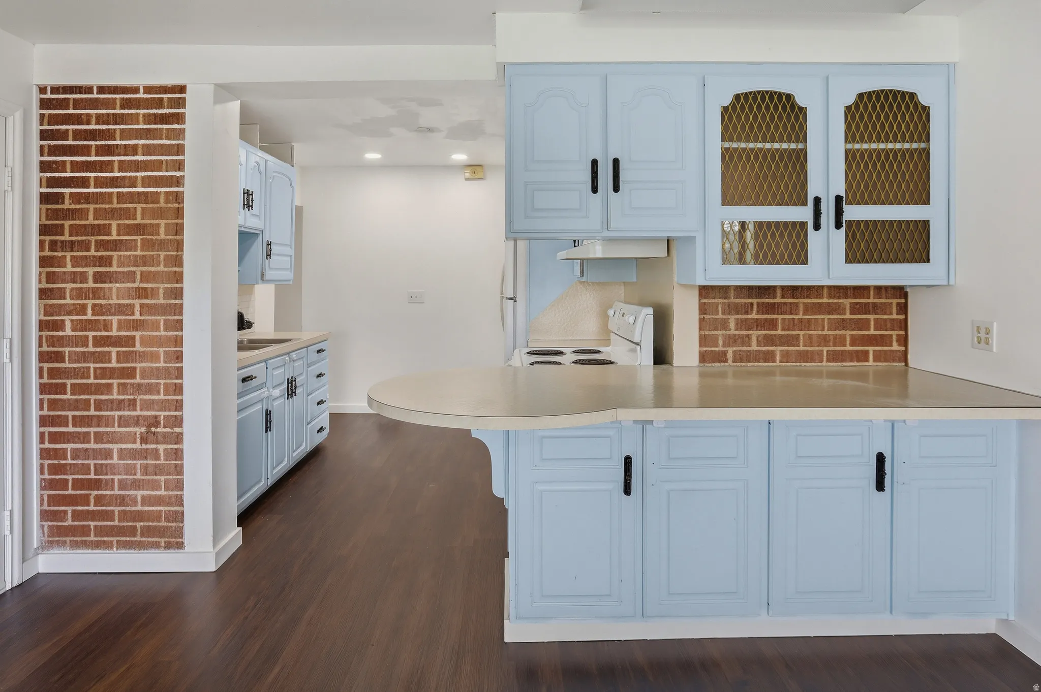Kitchen area featuring light blue cabinetry with dark hardware and a curved peninsula countertop
