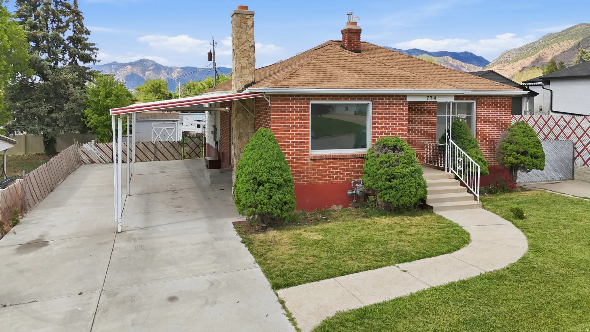 Brick exterior with a stone chimney, covered carport, concrete driveway, and a front walkway leading to the entry