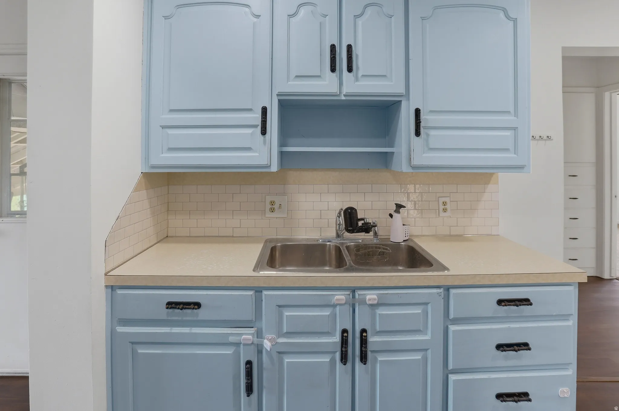 Kitchen area featuring light blue cabinetry with black hardware, a double basin stainless steel sink, and a white subway tile backsplash