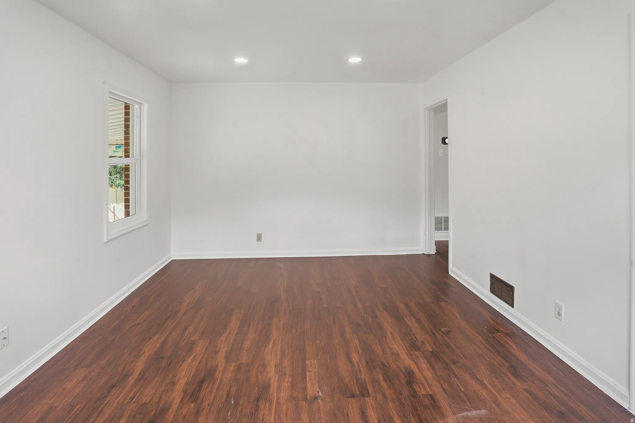 Spacious room featuring rich wood-finish flooring, crisp white walls, and recessed lighting