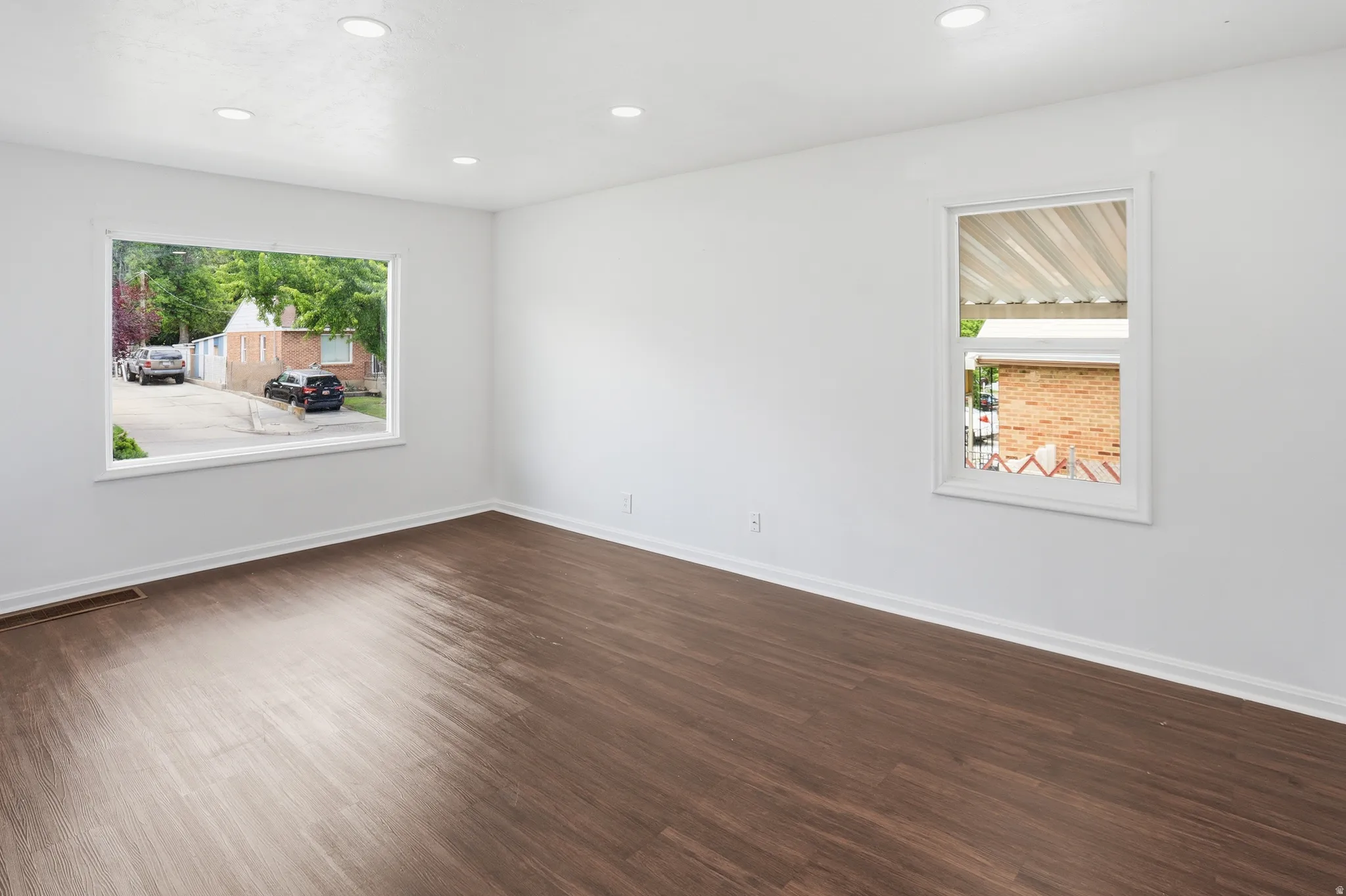 Spacious interior room featuring wood-finish flooring, crisp white walls, and recessed lighting