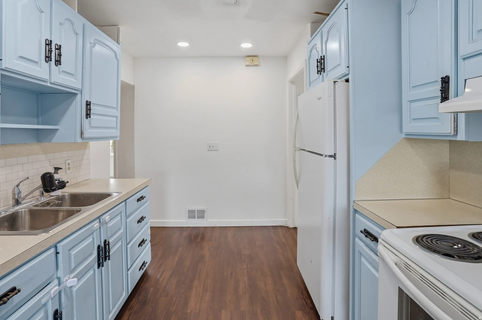 Kitchen featuring light blue cabinetry with dark hardware, a dual basin stainless steel sink, and wood-finish flooring