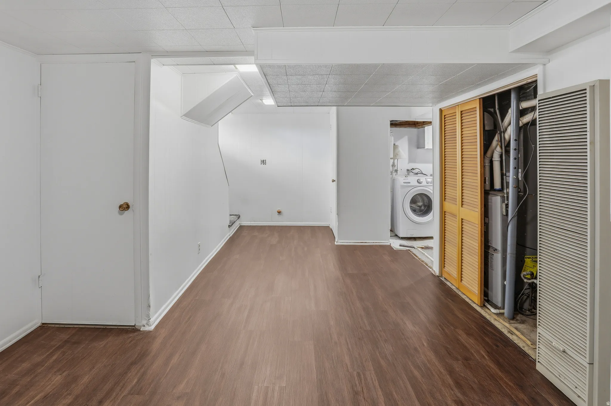 Open floor plan featuring wood-finish flooring, white walls, and a recessed laundry area with a visible washer