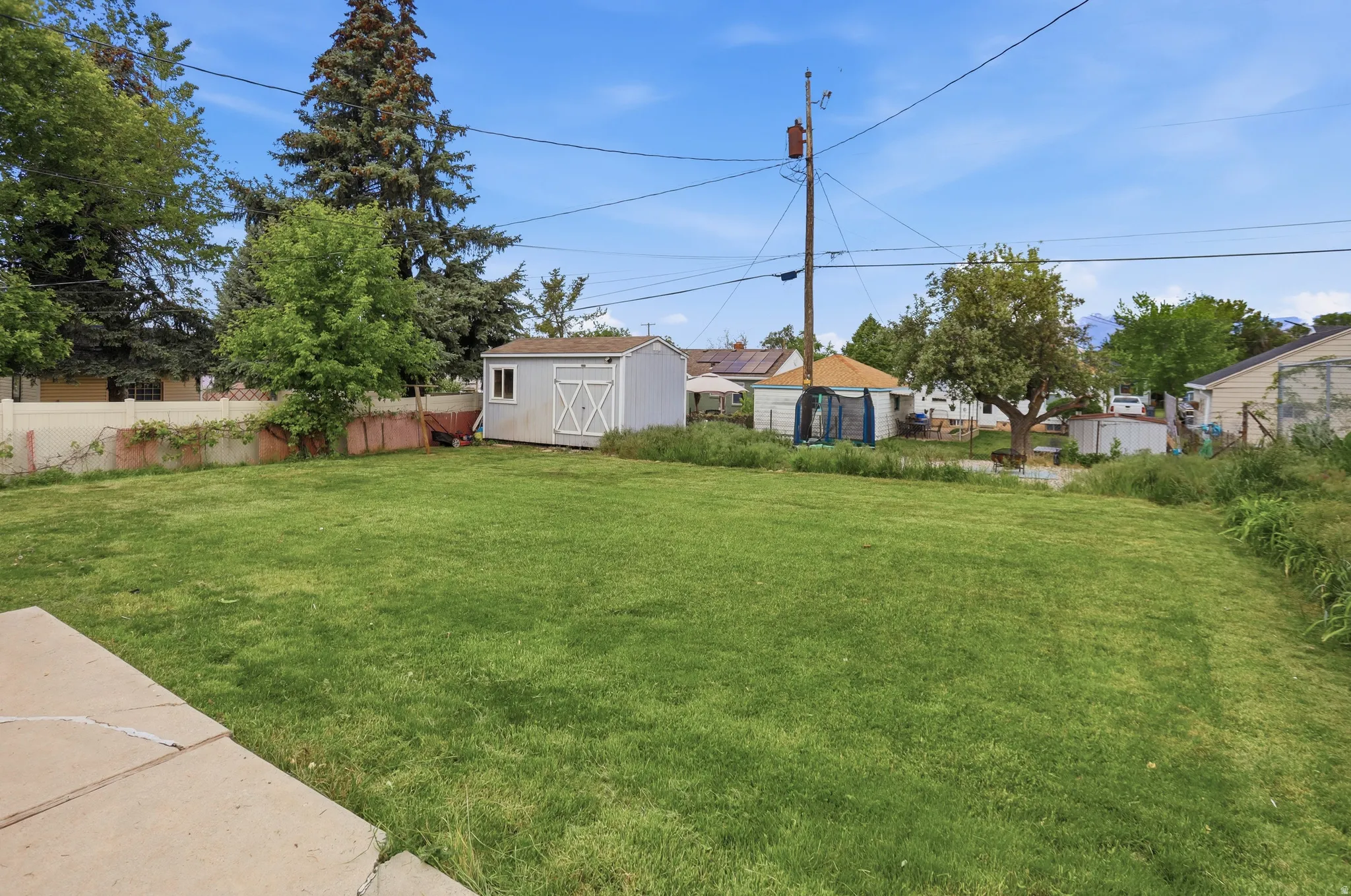 Expansive green lawn area featuring a detached storage shed, mature perimeter trees, and a partial privacy fence