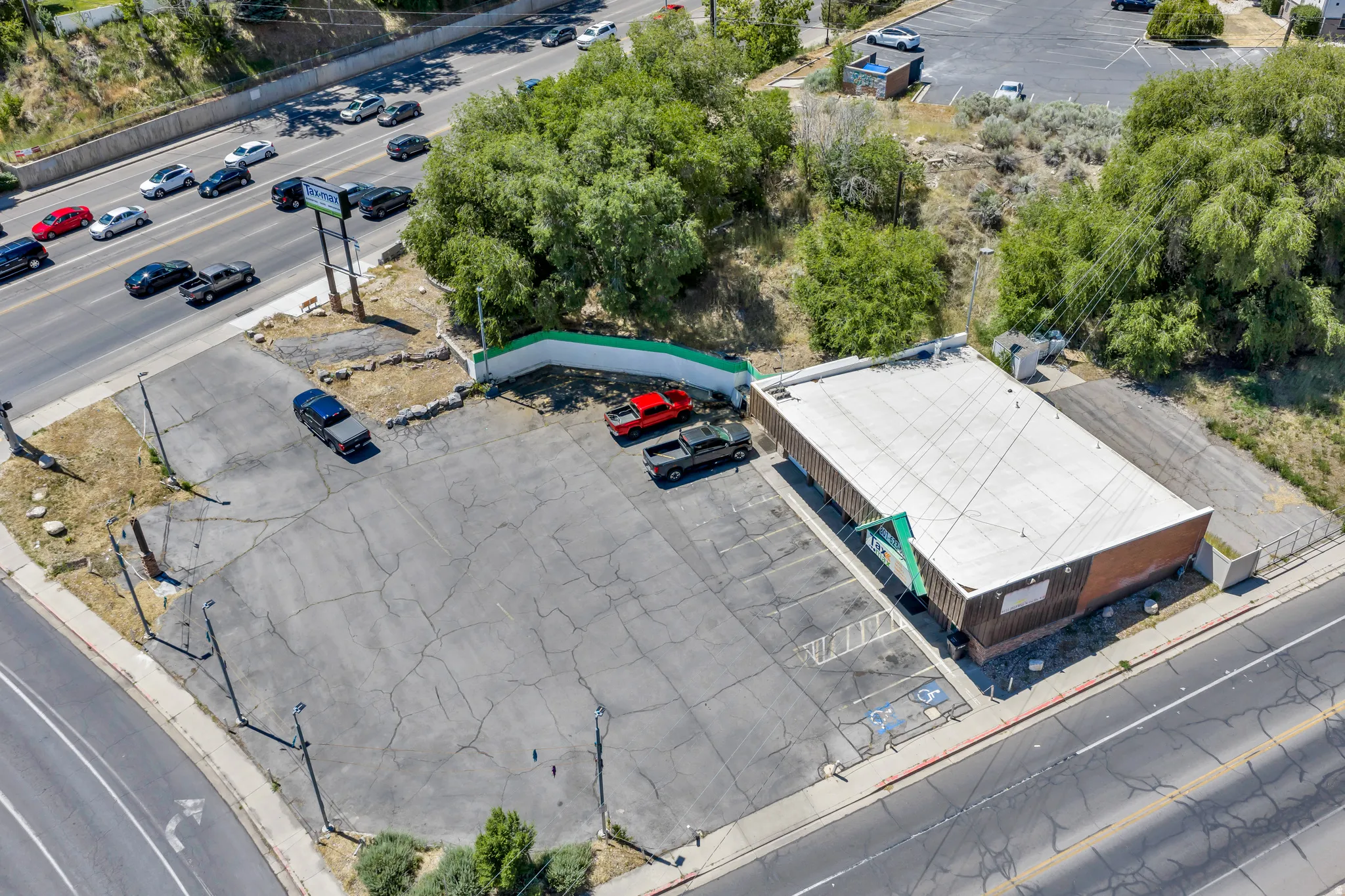 Commercial building with a flat roof, featuring a paved parking lot, a prominent road-facing sign structure, and a retaining wall
