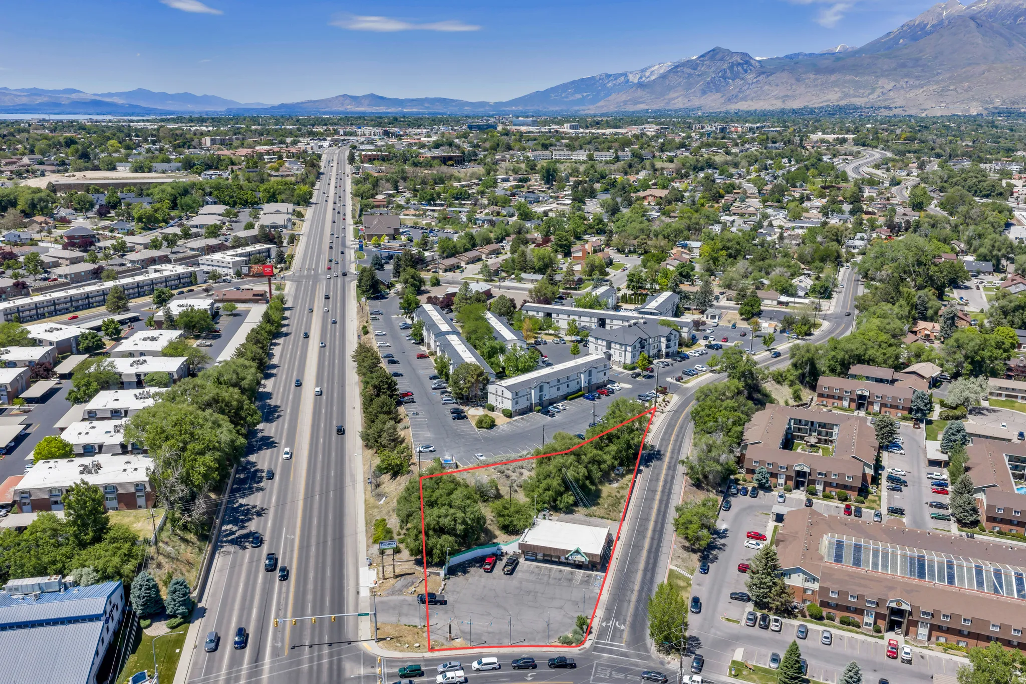 Aerial perspective showcasing a commercial property with a paved parking lot and single-story building, situated at a road intersection