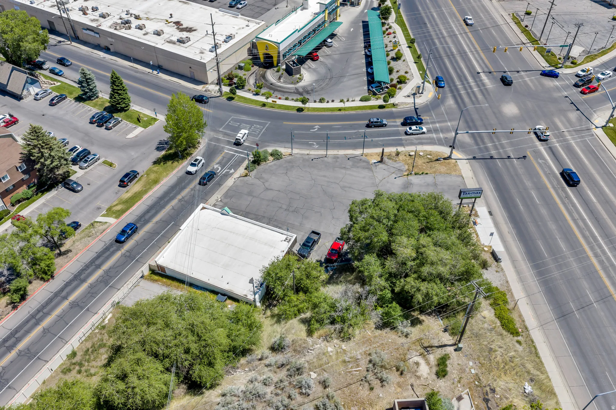 Vacant commercial lot featuring a partial structure, surrounded by mature trees and paved areas