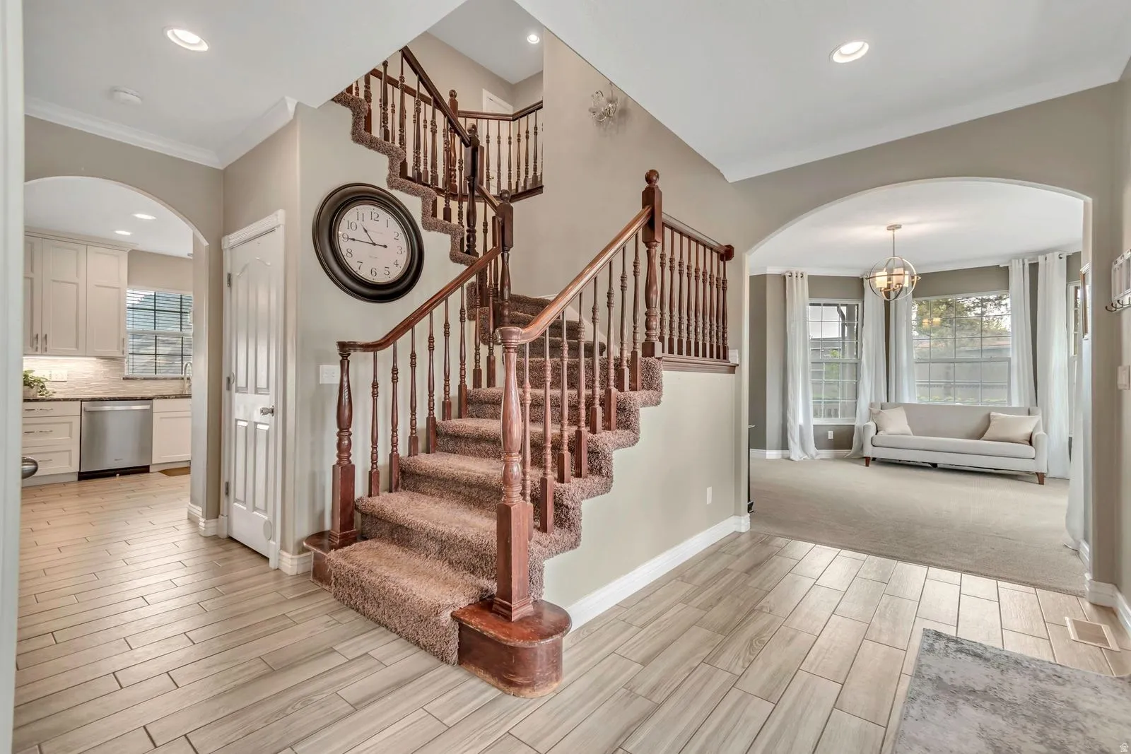 Grand staircase featuring dark wood balusters and carpeted treads, complemented by light wood-finish flooring